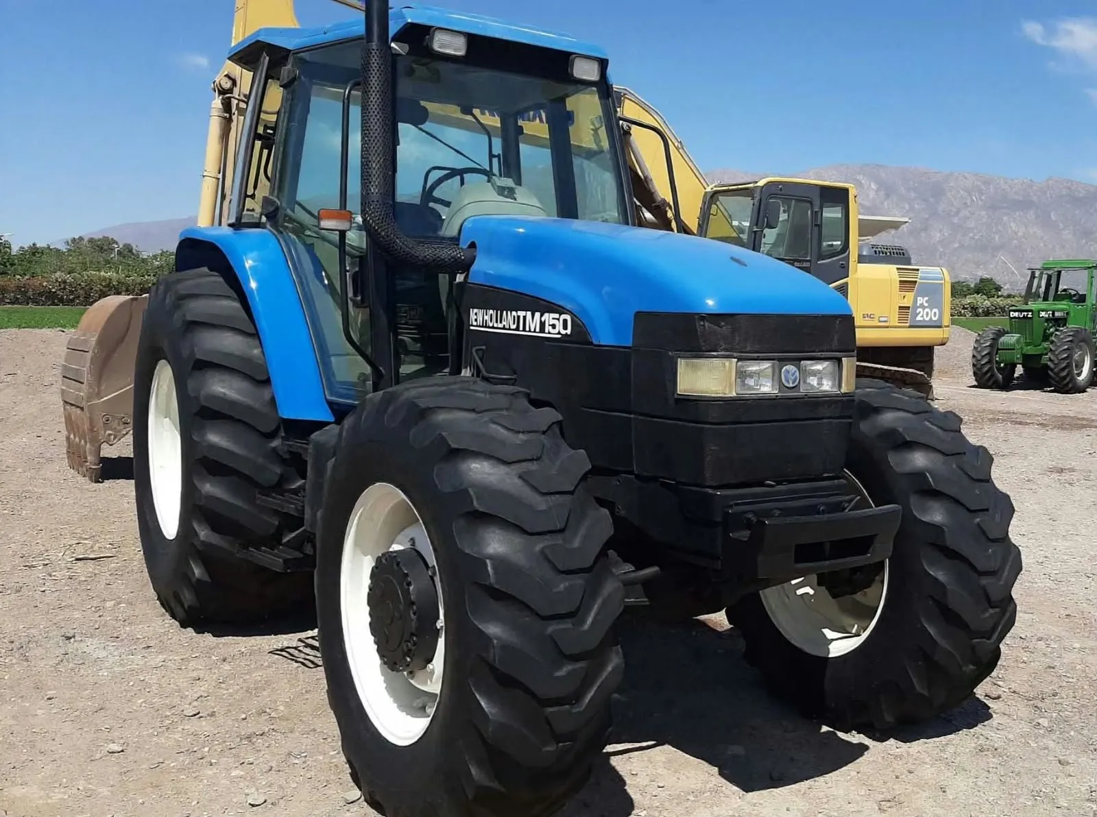 Tractor New Holland azul con excavadoras y montañas al fondo